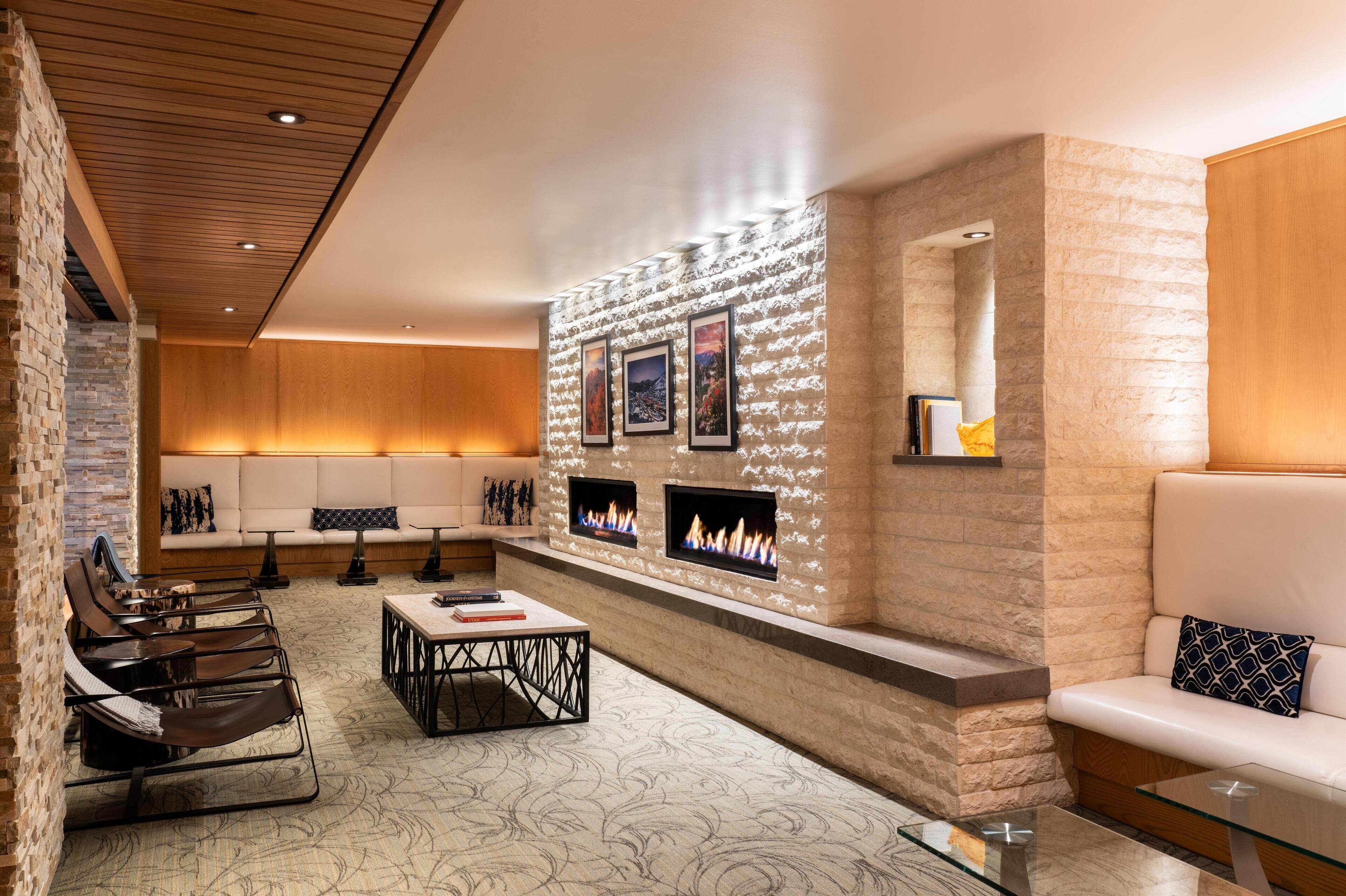 A modern lounge area with a stone wall, fireplace, seating, and a patterned carpet.