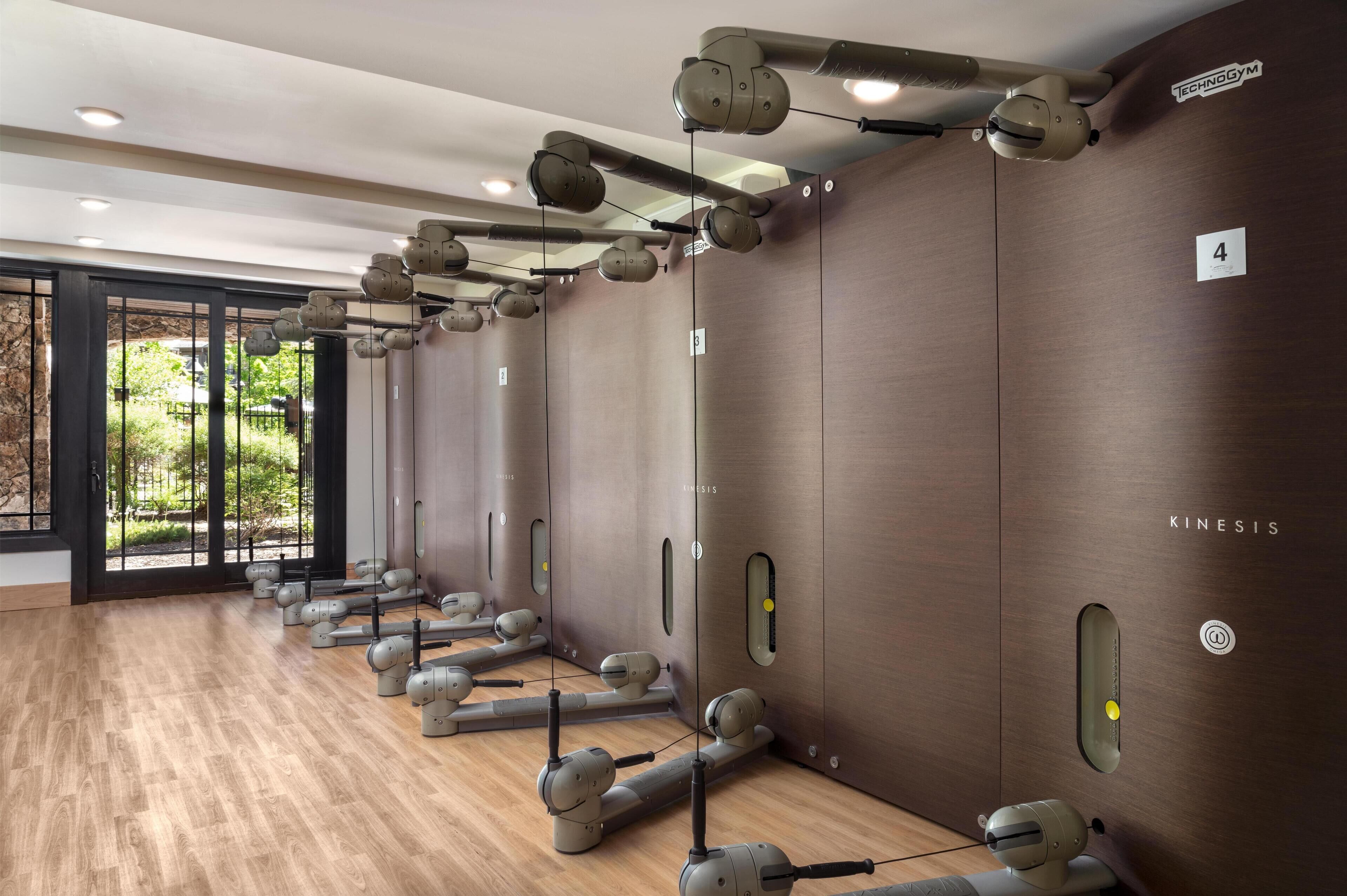 Un gimnasio con equipo de ejercicio, pisos de madera y grandes ventanales.