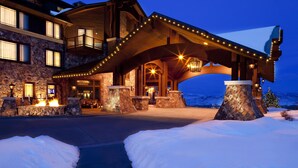A large, multi-story building with a stone facade, a covered entrance area with a wooden arch, and a snow-covered ground. - Waldorf Astoria Park City (Park City)