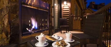 A glass-top table with dessert plates and cups, a stone wall, a fireplace, and a wicker chair.
