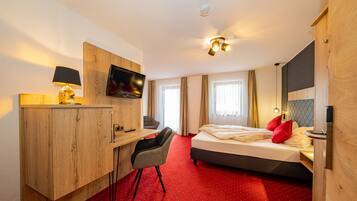 Habitación de hotel con un escritorio de madera, televisor, cama con almohadas rojas y alfombra roja.