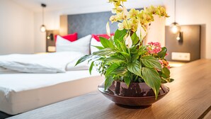 A modern hotel room with a bed, a bedside table with a potted plant, and a view of the sky through the window. - Berggasthof Hotel Adersberg (Grassau)