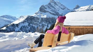 Una persona sentada en un banco de madera en un paisaje nevado, con una montaña al fondo.