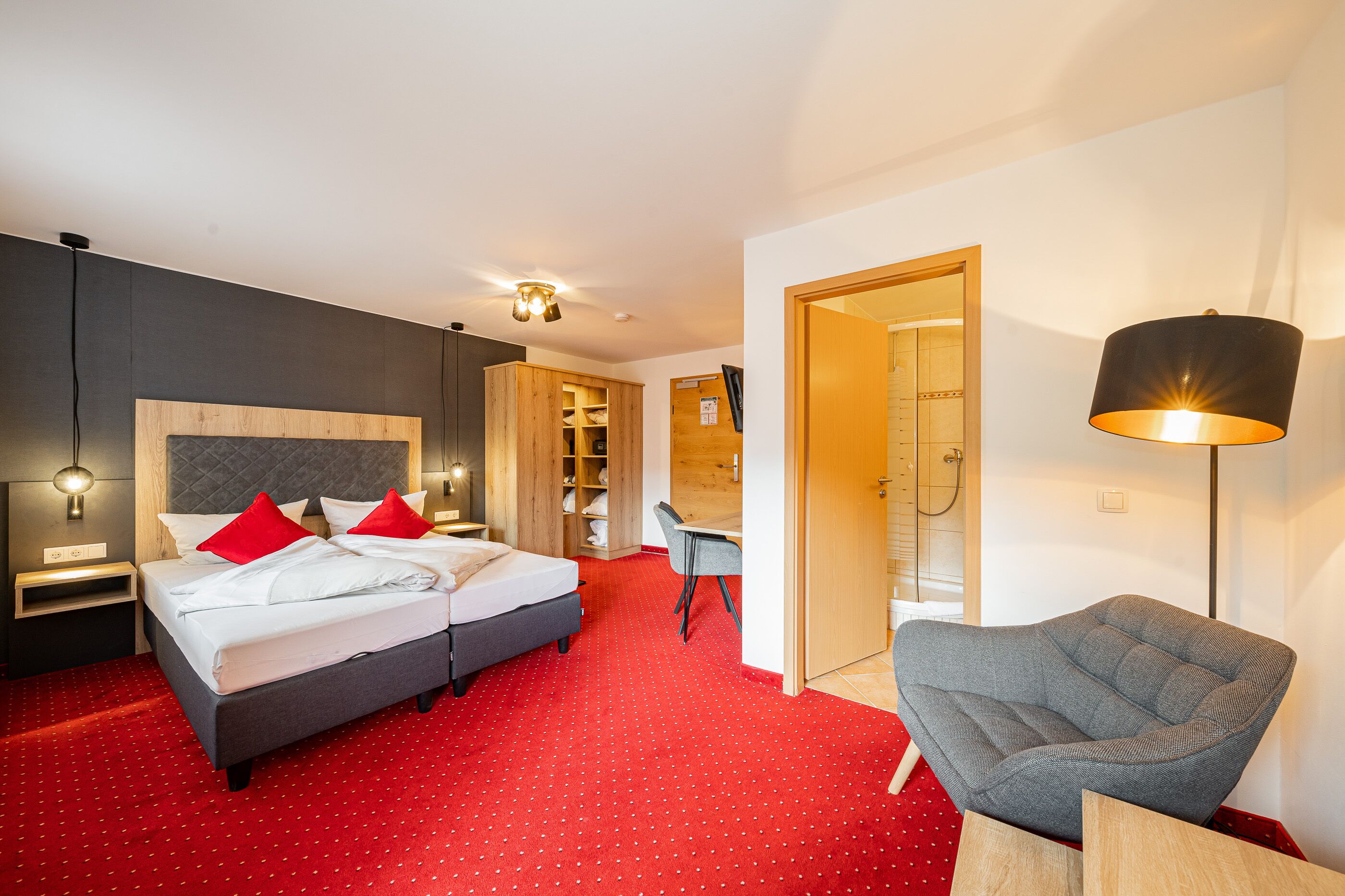 A hotel room with a bed, two bedside tables, a desk, a chair, and a shower area.