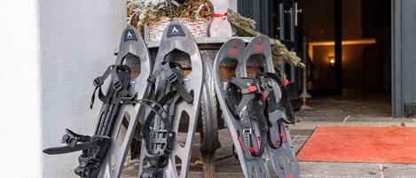 Three pairs of skis leaning against a wall, a potted plant, and a red carpet leading to a door.