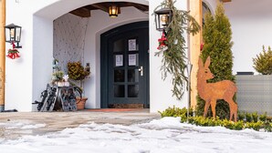 A snow-covered entrance with a black door, a wooden archway, and a metal deer decoration. - Berggasthof Hotel Adersberg (Grassau)