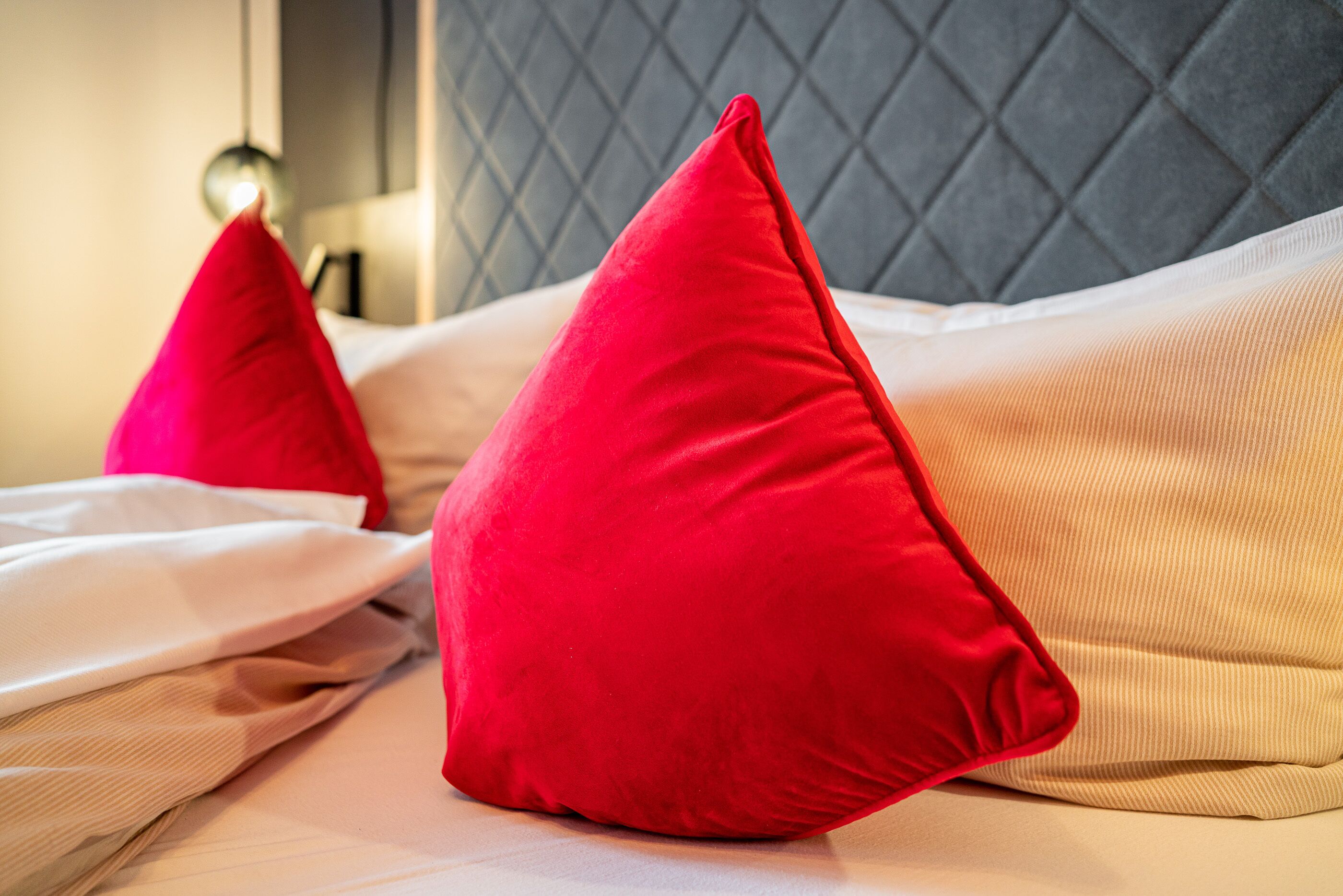 A bed with two red pillows and a grey headboard.