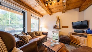 A cozy living room with a wooden ceiling, a sofa set, a coffee table, a television, and a small cabinet. - Berggasthof Hotel Adersberg (Grassau)