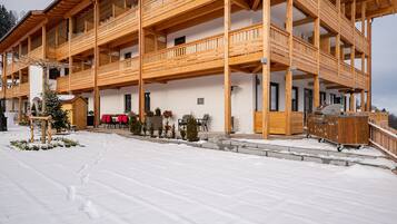 Un edificio de madera de varios pisos con balcones, un área de estar cubierta al aire libre y suelo cubierto de nieve.
