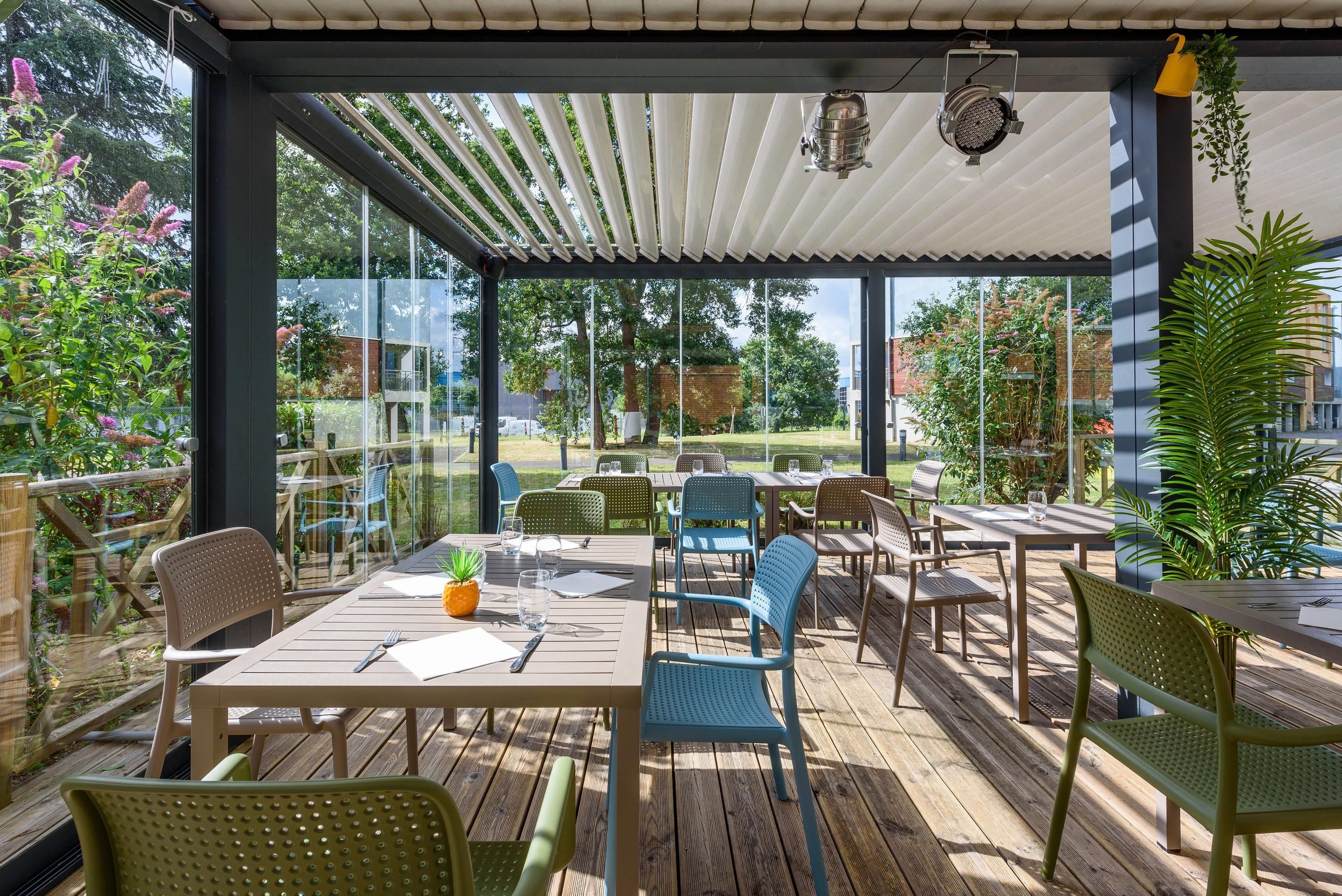 Une terrasse extérieure avec des tables et des chaises en bois, une pergola et des plantes en pot.
