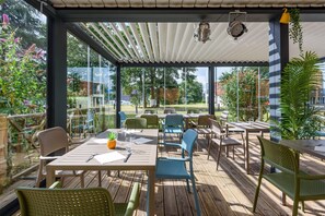 Une terrasse extérieure avec des tables et des chaises en bois, une pergola et des plantes en pot.