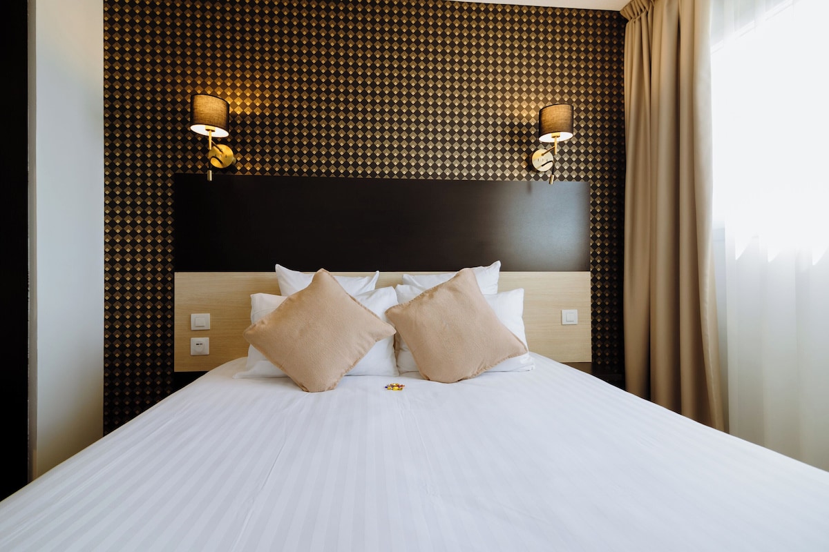 A hotel room with a large bed, two wall-mounted lamps, and a textured wall behind the bed.