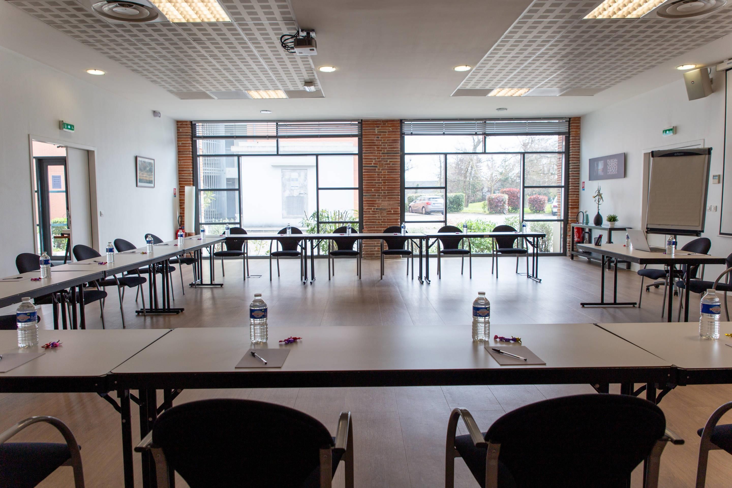 A conference room with long tables, chairs, water bottles, and a projector.