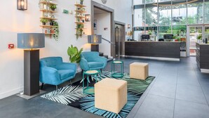 Un hall d’entrée moderne avec un comptoir d’accueil, des fauteuils bleus, une grande fenêtre et un mur végétal.