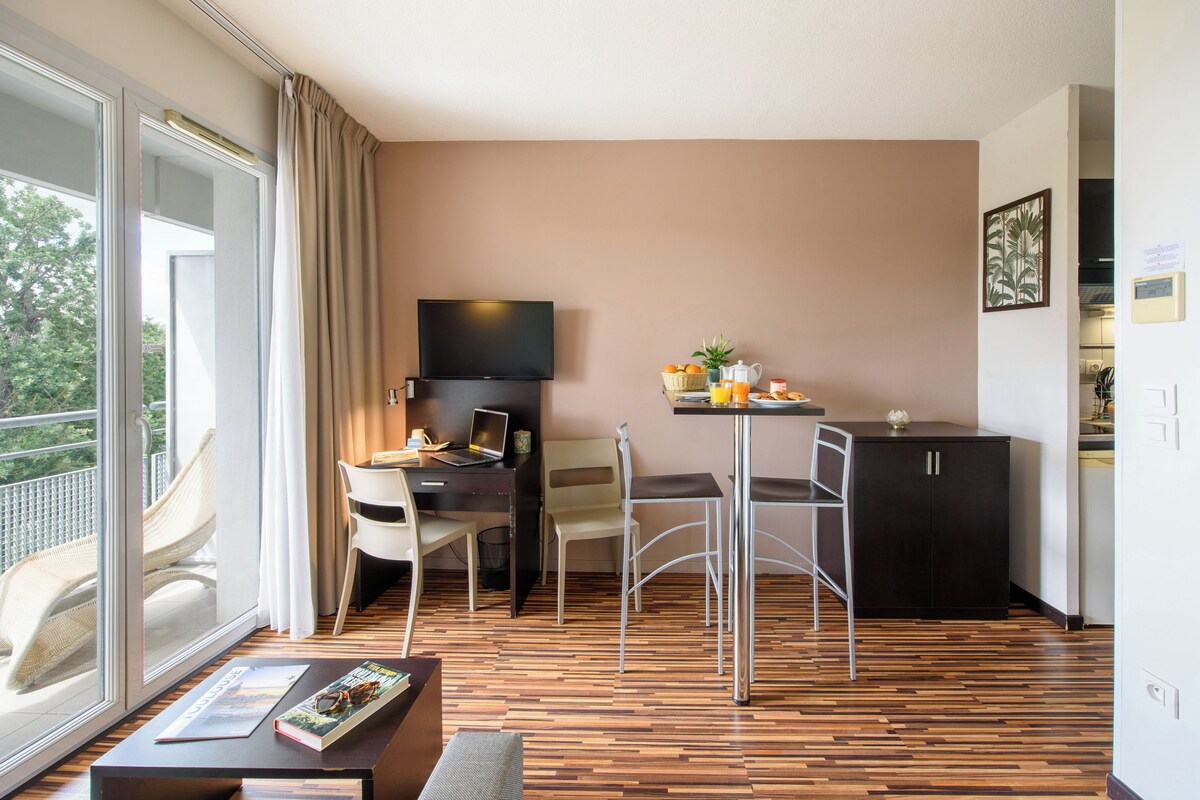 Une chambre d’hôtel moderne dotée d’un balcon, d’un coin repas, d’une télévision à écran plat et d’une kitchenette.