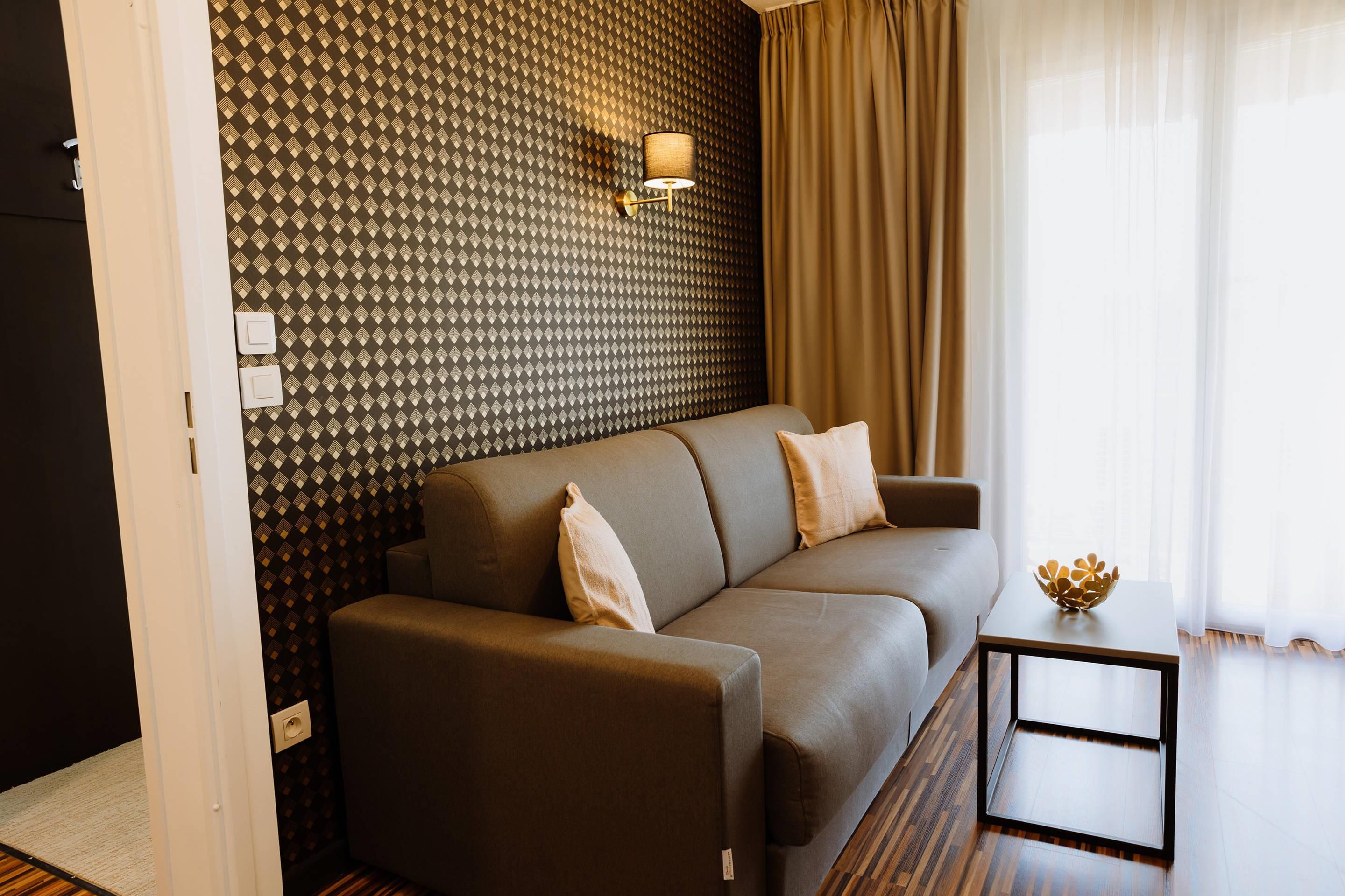 A modern living room with a patterned wall, a sofa, a side table, and a lamp.