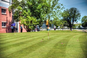A well-maintained grassy area with a flagstick, likely a putting green, and a few scattered golf balls.