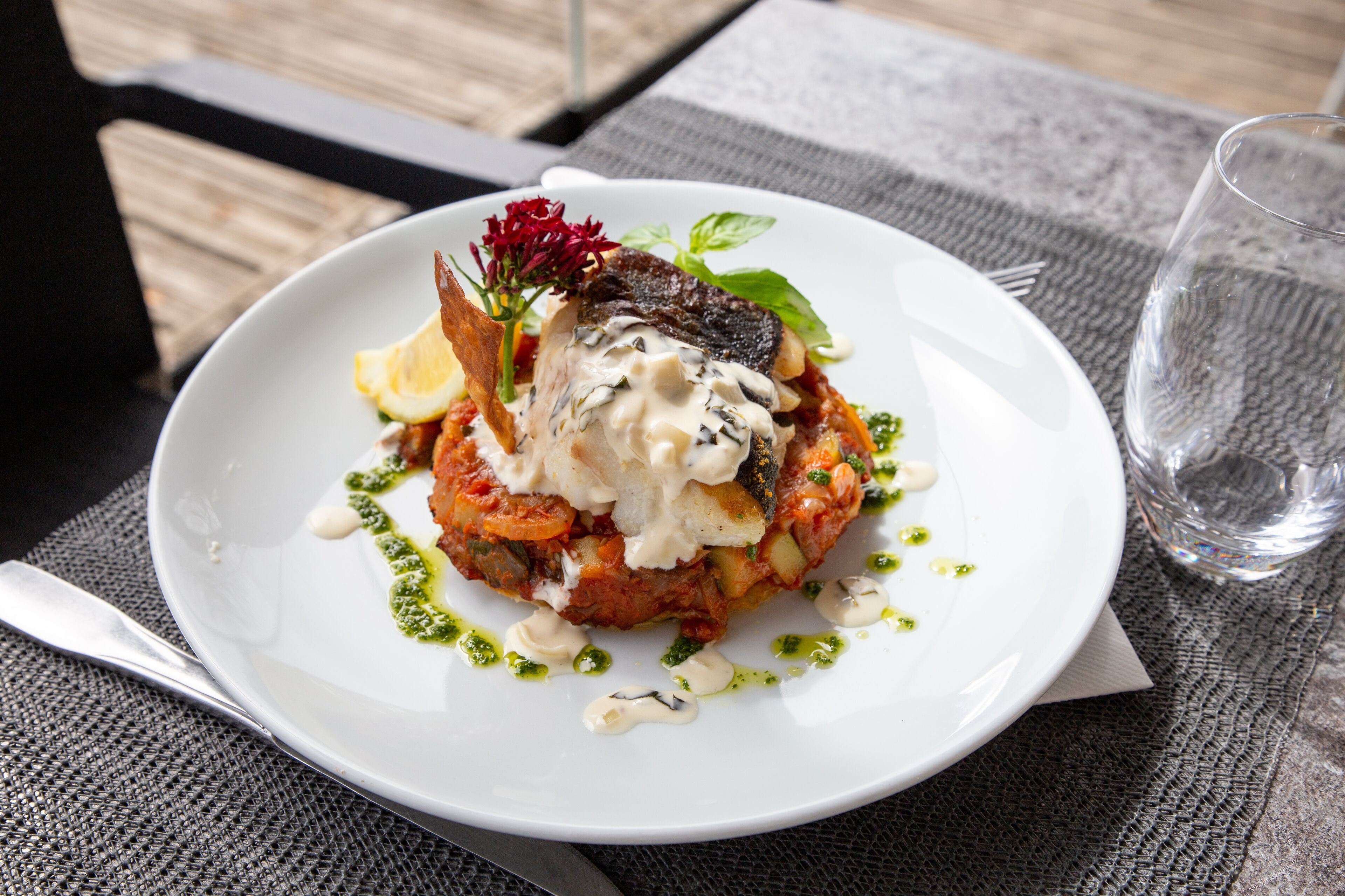 A white plate with a dish of food, a glass of water, and a spoon on a table.