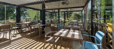 Un patio al aire libre con suelo de madera, mesas, sillas y una sección cubierta con techo blanco.