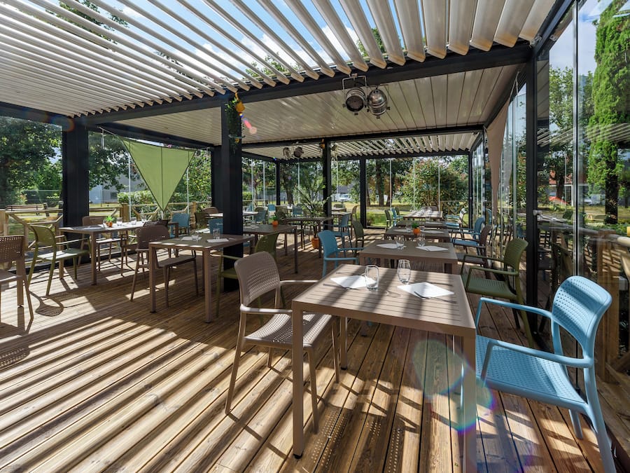 An outdoor patio area with wooden flooring, tables, chairs, and a covered section with a white roof.