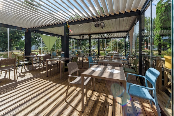 Un patio al aire libre con suelo de madera, mesas, sillas y una sección cubierta con techo blanco.