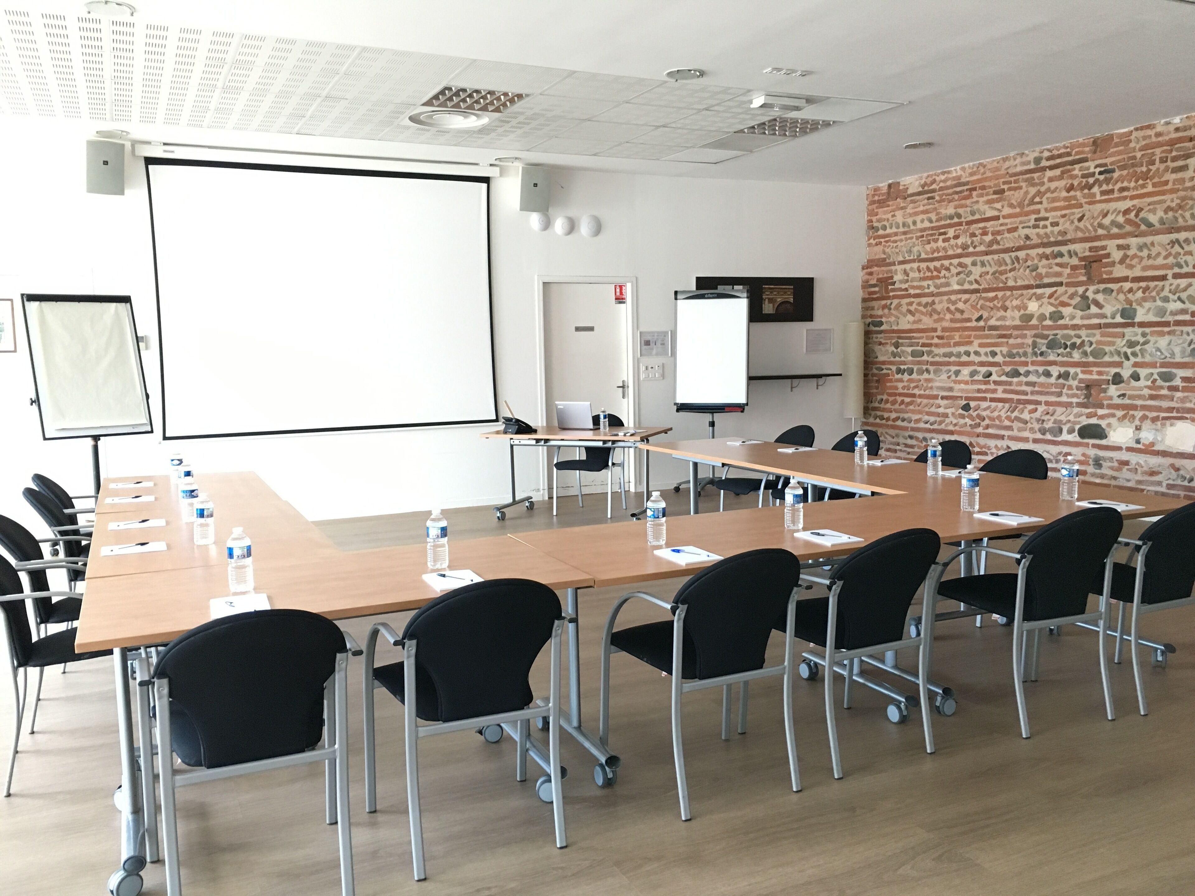 Ett konferensrum med ett långt bord, svarta stolar, en projektorduk och en whiteboard.