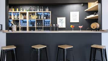 Zona de bar con pared oscura, estantes llenos de botellas de licor y dos taburetes.
