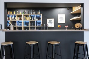 A bar area with a dark wall, shelves of liquor bottles, and two stools.