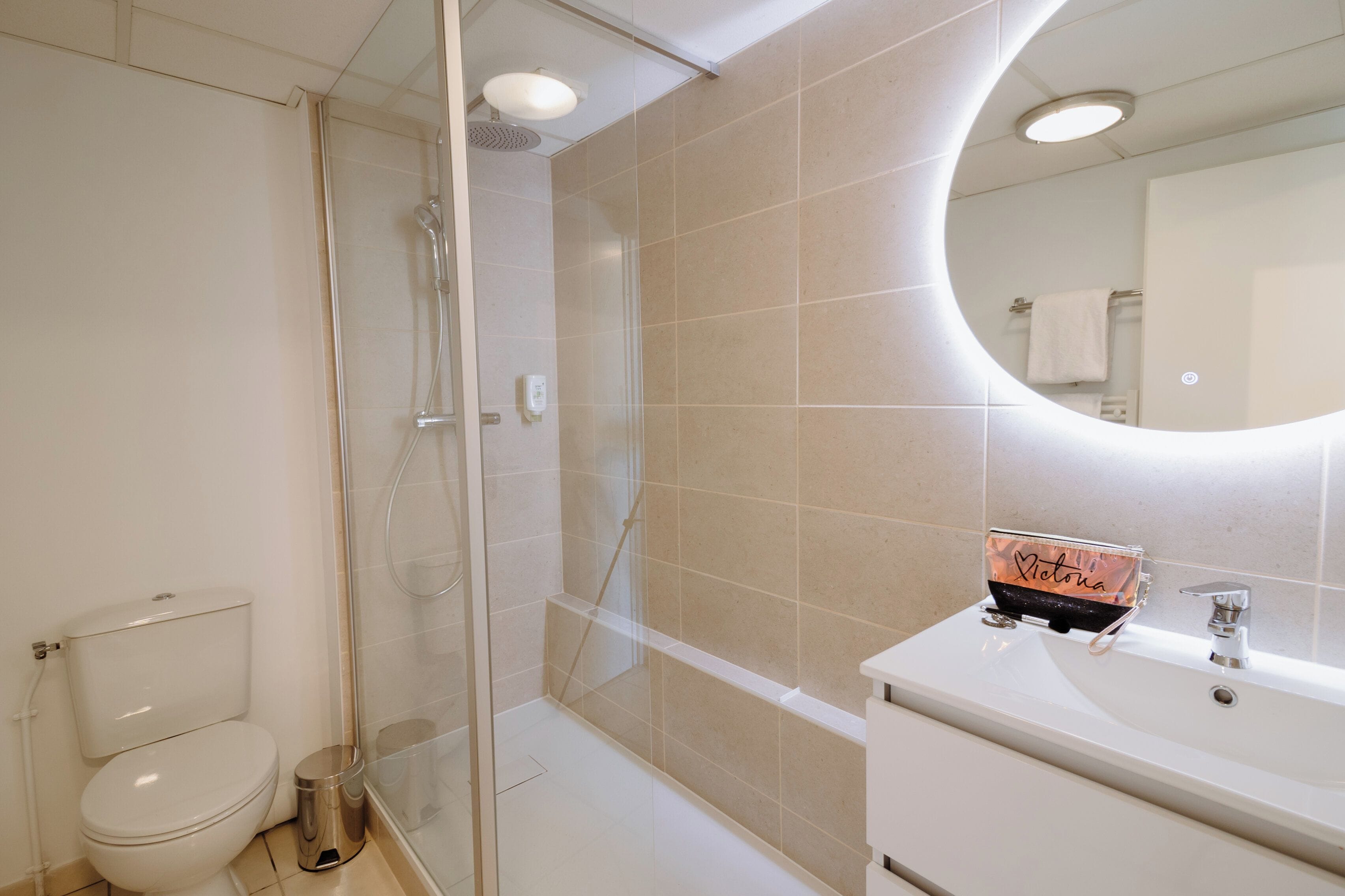 A modern bathroom with a glass shower enclosure, a toilet, a sink, and a mirror with a round frame.