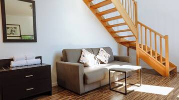 A modern living room with a wooden staircase, a sofa with cushions, a side table, and a dark wooden dresser.