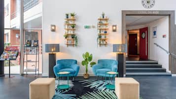 Un vestíbulo con dos sillones azules, un tapete con estampado negro y verde, y estanterías de madera con plantas.