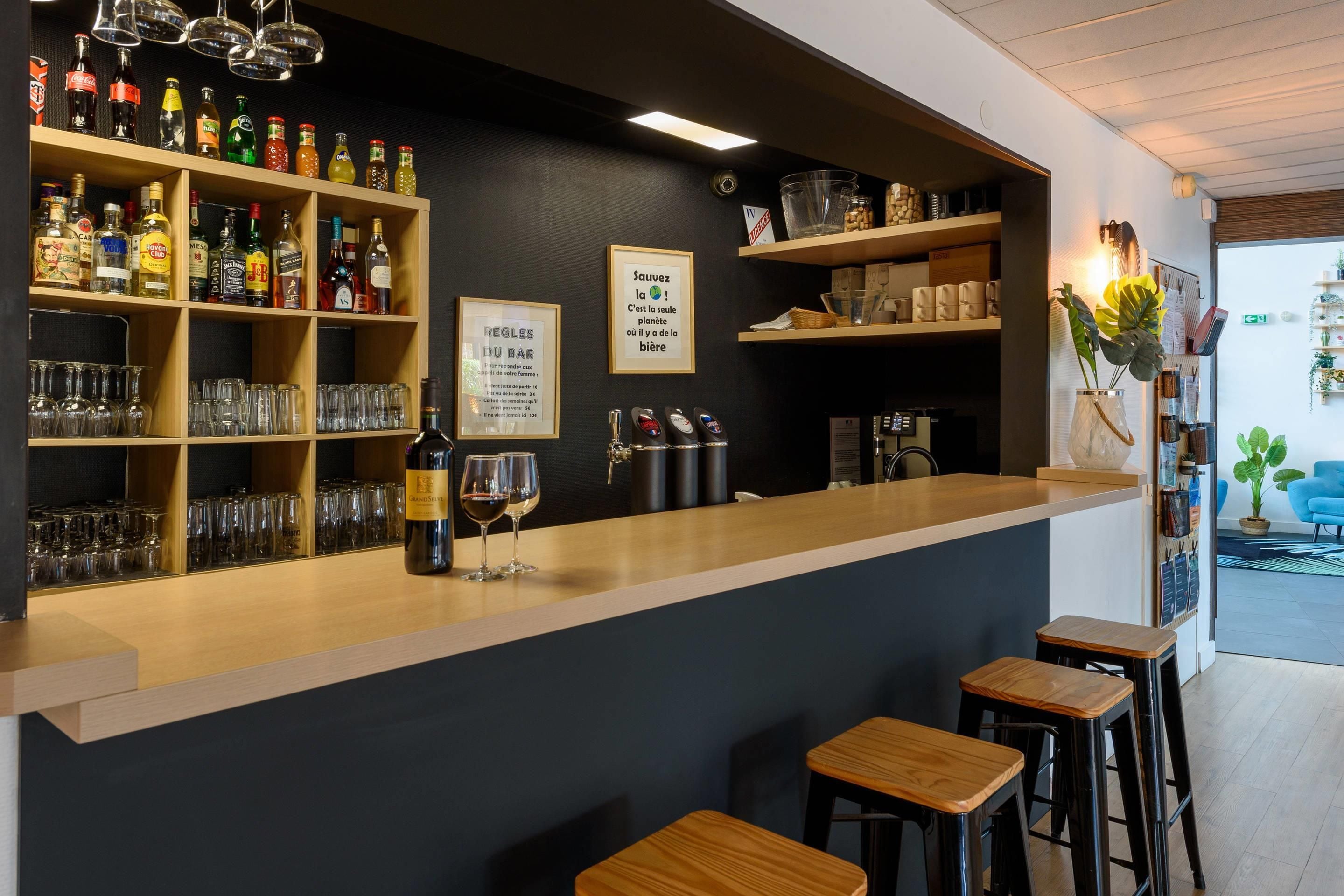 A bar area with shelves of bottles and glasses, a wine bottle, and a sign with rules.