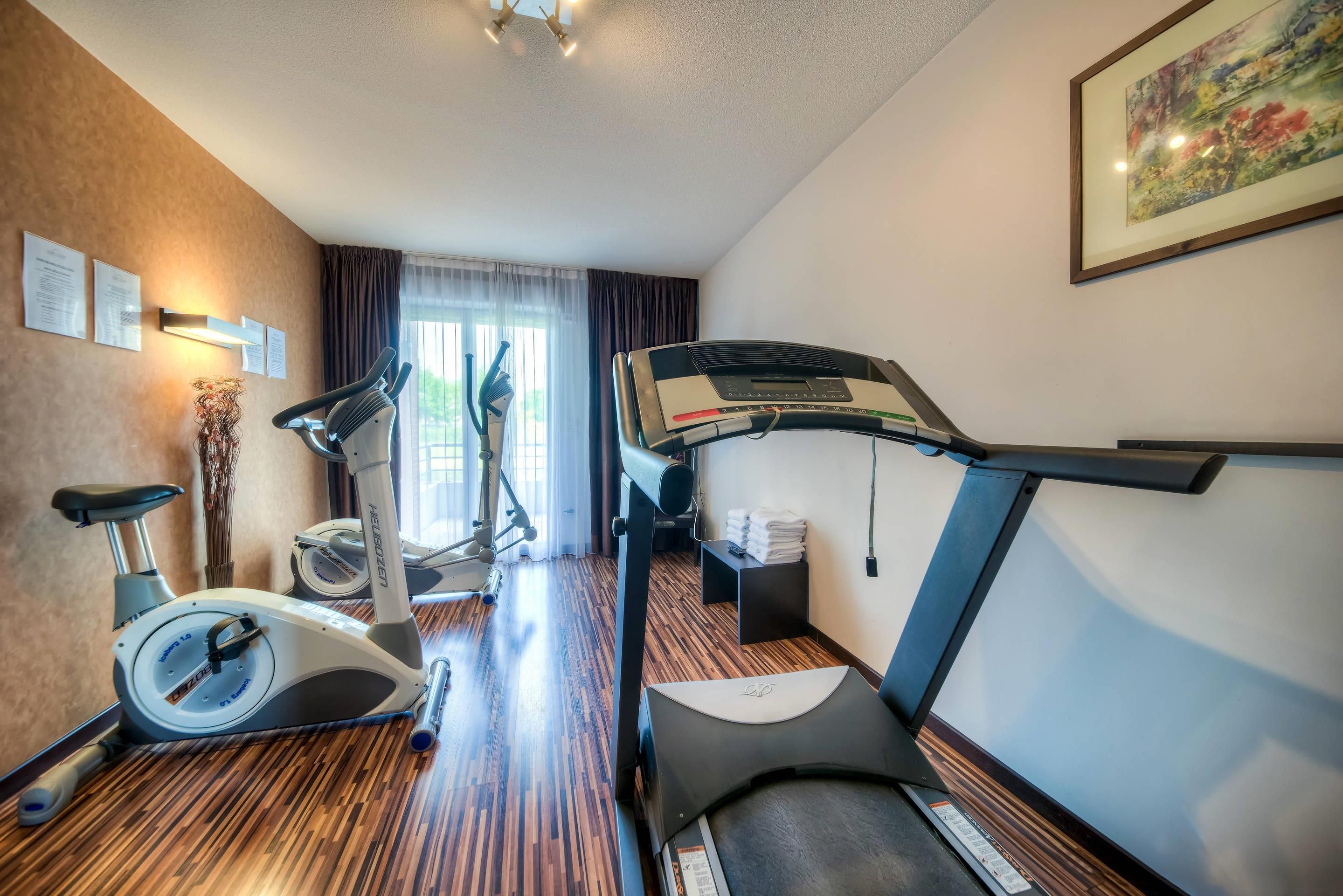Hotelkamer met loopband, hometrainer en raam met gordijnen.