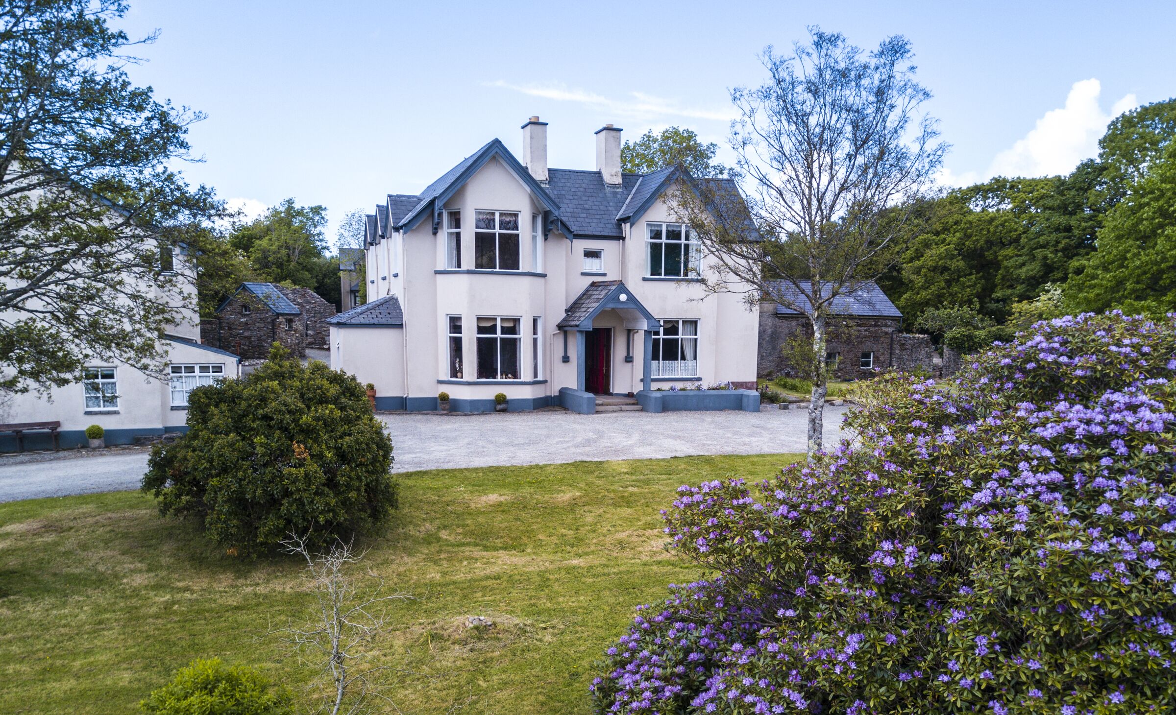 A large, two-story house with a prominent entrance, surrounded by well-maintained gardens and trees.