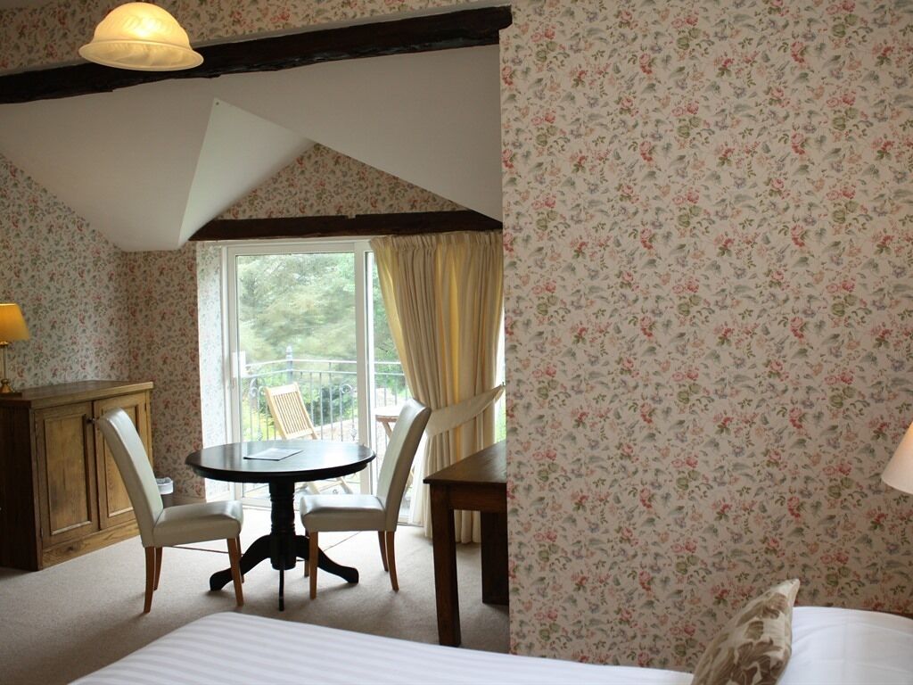 A bedroom with a bed, a round table, two chairs, a wooden cabinet, and a balcony with curtains.