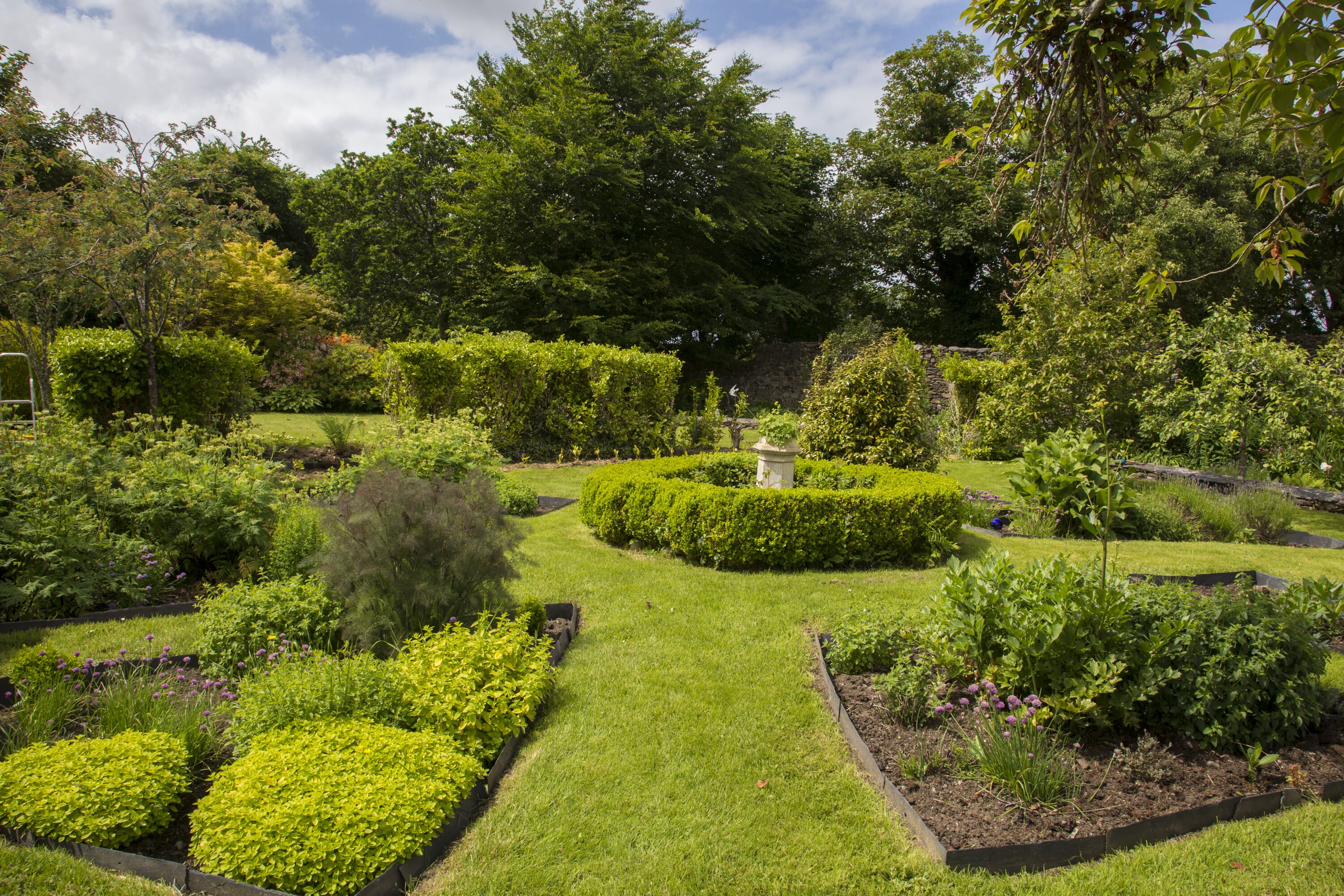 A well-maintained garden with various plant beds and a central stone structure.