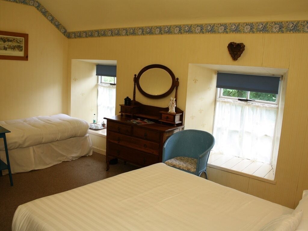 Un dormitorio con dos camas, un tocador, una silla, un espejo y dos ventanas con cortinas.