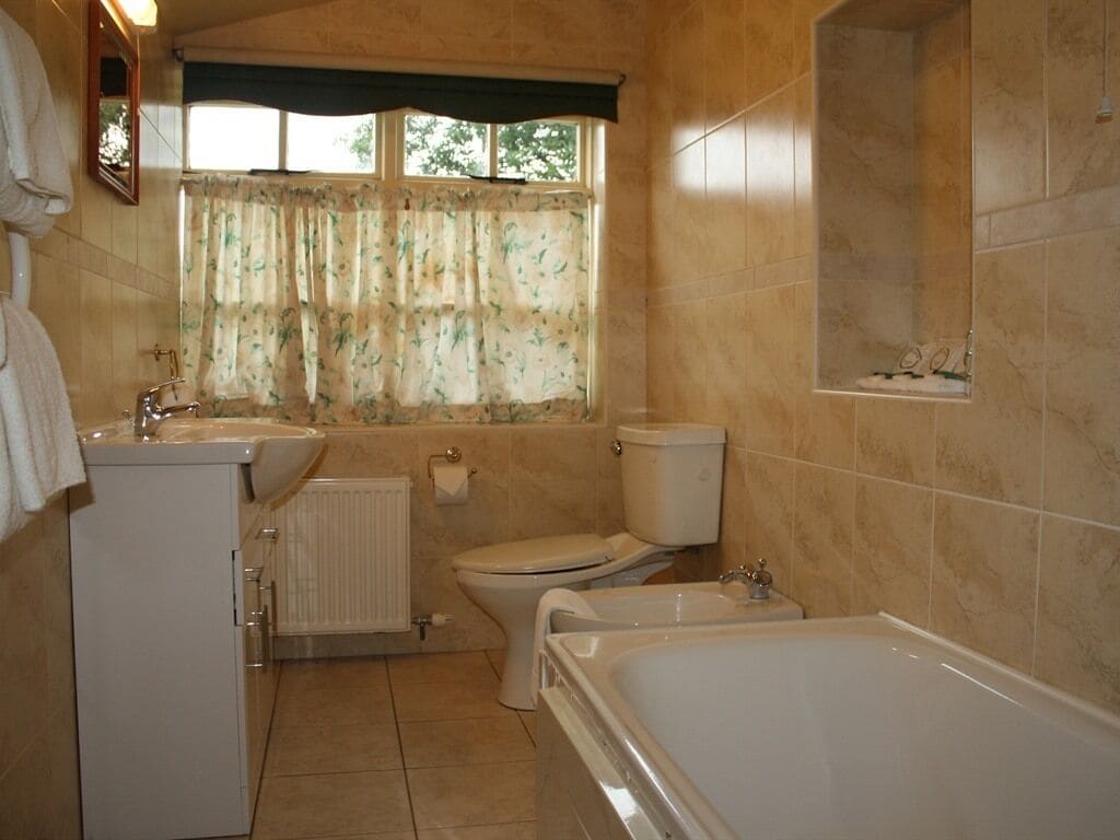Ein Badezimmer mit Toilette, Waschbecken, Badewanne und einem Fenster mit blumigem Vorhang.