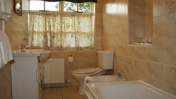A bathroom with a toilet, sink, bathtub, and a window with floral curtains.