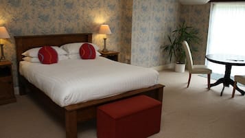 Une chambre à coucher avec un grand lit, deux lampes de chevet, un pouf rouge, une table ronde et une plante en pot.