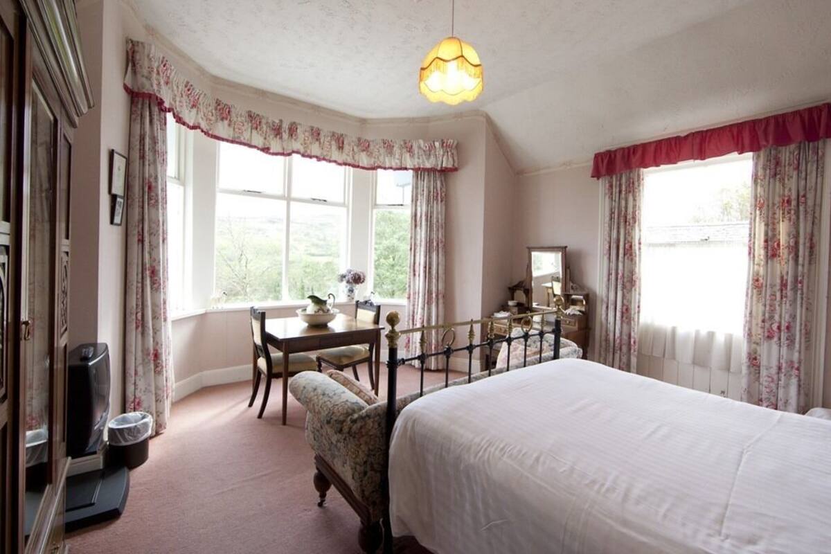 Ein Schlafzimmer mit einem großen Bett, einem Schreibtisch mit Stuhl und einem Fenster mit Vorhängen.