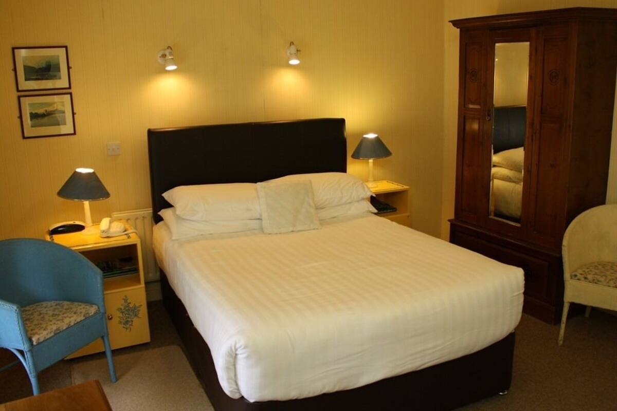 Ein Hotelzimmer mit einem großen Bett, zwei Nachttischlampen, einem Holzschrank, einem blauen Sessel und einem kleinen Tisch.