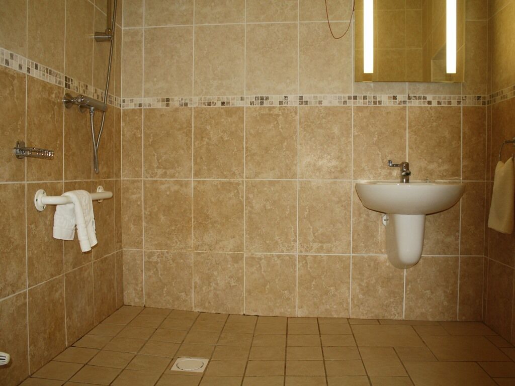 Un baño con baldosas color beige, un lavamanos blanco y una ducha.