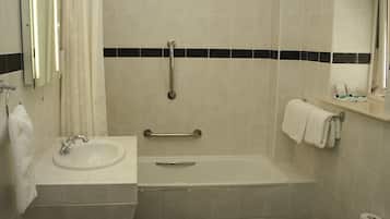 Un baño con lavamanos, espejo, bañera y barra de apoyo.