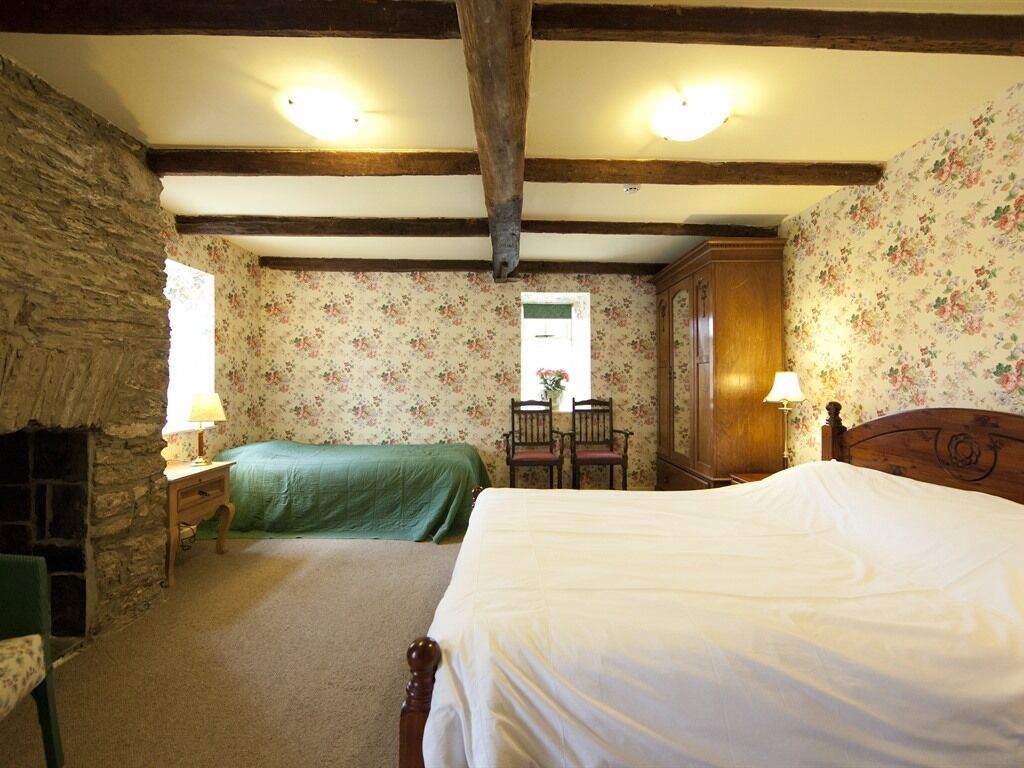 Een slaapkamer met twee bedden, een stenen muur, bloemenbehang en een houten plafond.