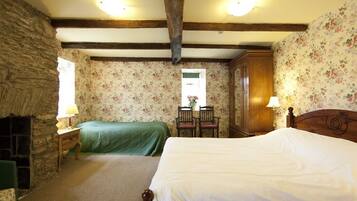 Een slaapkamer met twee bedden, een stenen muur, bloemenbehang en een houten plafond.