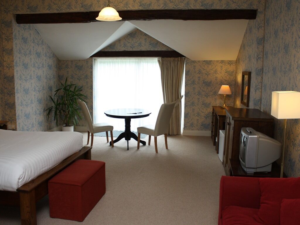Une chambre d’hôtel comprenant un lit, un bureau avec une télévision, une table à manger avec des chaises, un canapé rouge et une plante en pot.