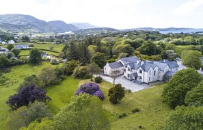 A large estate with a prominent house surrounded by lush greenery and rolling hills. - Woodhill House (Ardara)