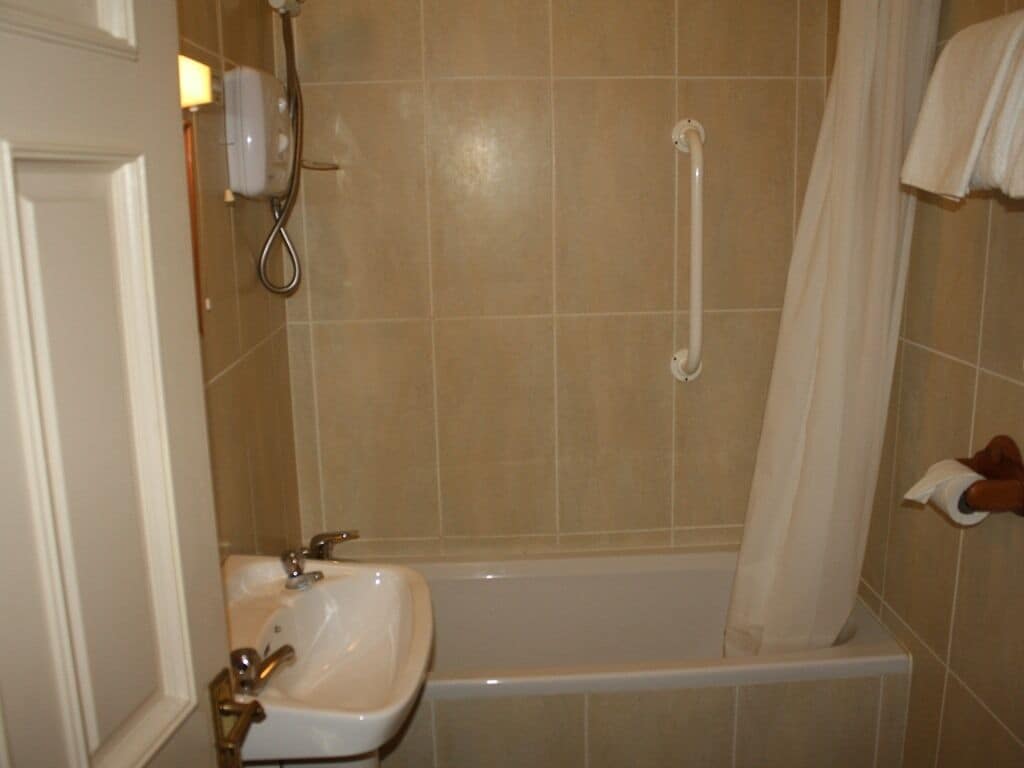 A bathroom with a bathtub, a sink, a showerhead, and a handrail.