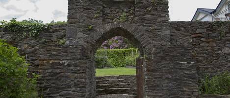 A stone archway leading to a grassy area with a wooden gate.